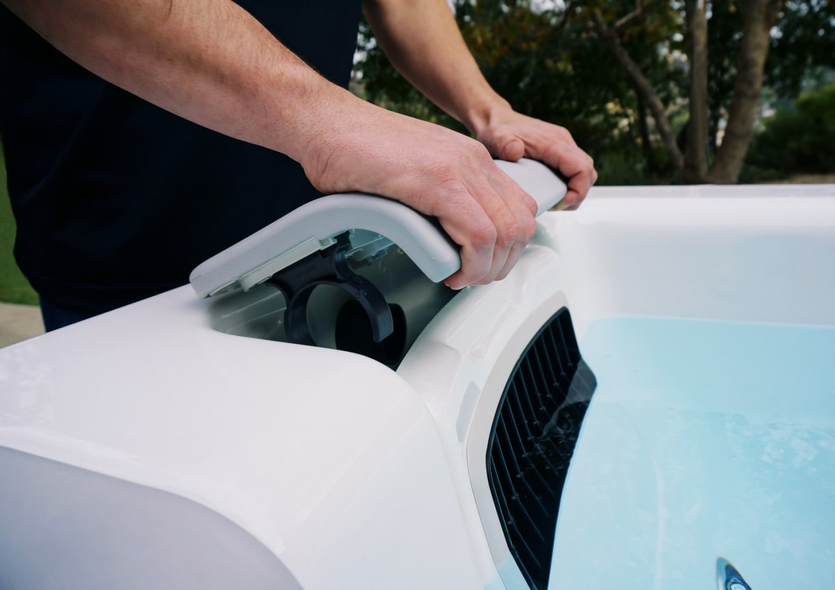 A man is removing something from the side of a hot tub.